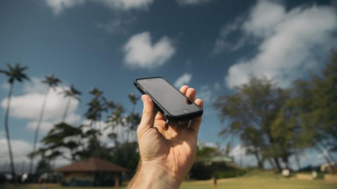 Telephone Personne qui tient dans sa main un téléphone portable sur un fond de cocotiers et de ciel bleu