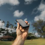 Personne qui tient dans sa main un téléphone portable sur un fond de cocotiers et de ciel bleu